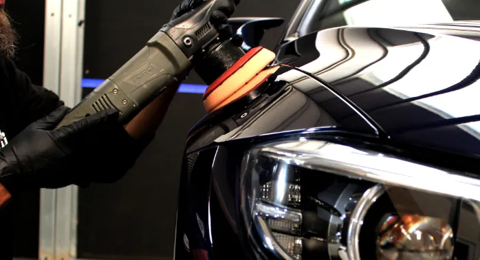 Dual action polisher removing swirl marks during paint correction on glossy black paint